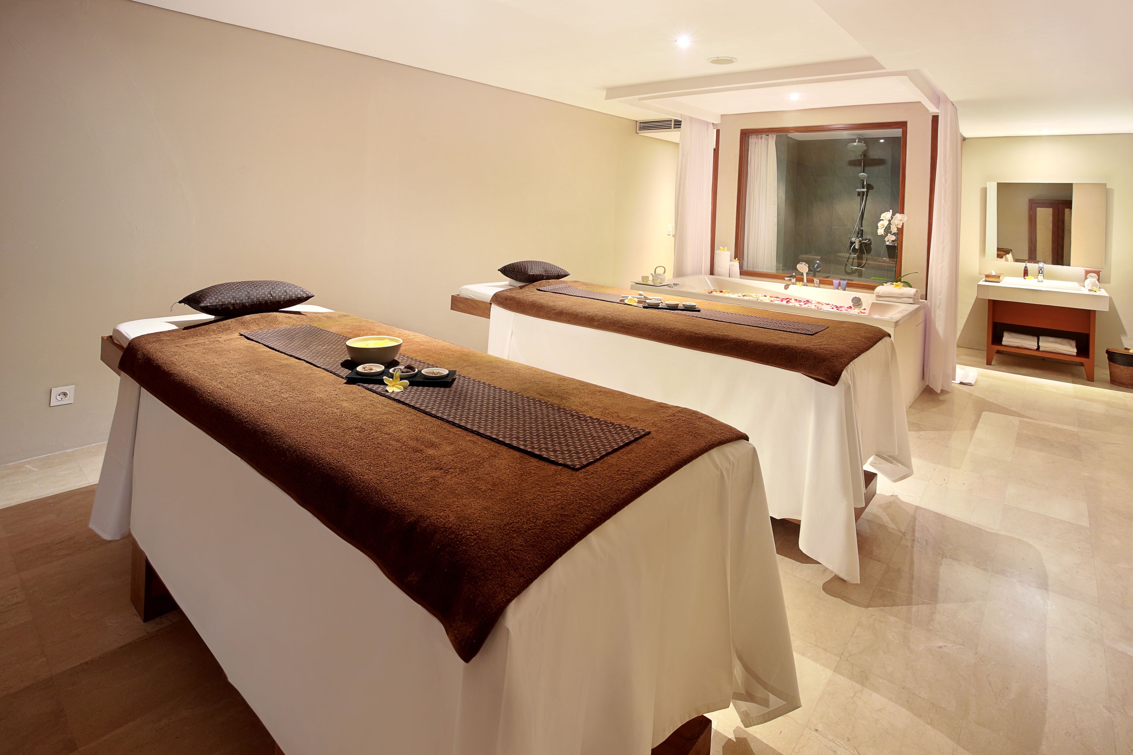 A spa room with two massage tables, each with a towel, pillow, and a mat.