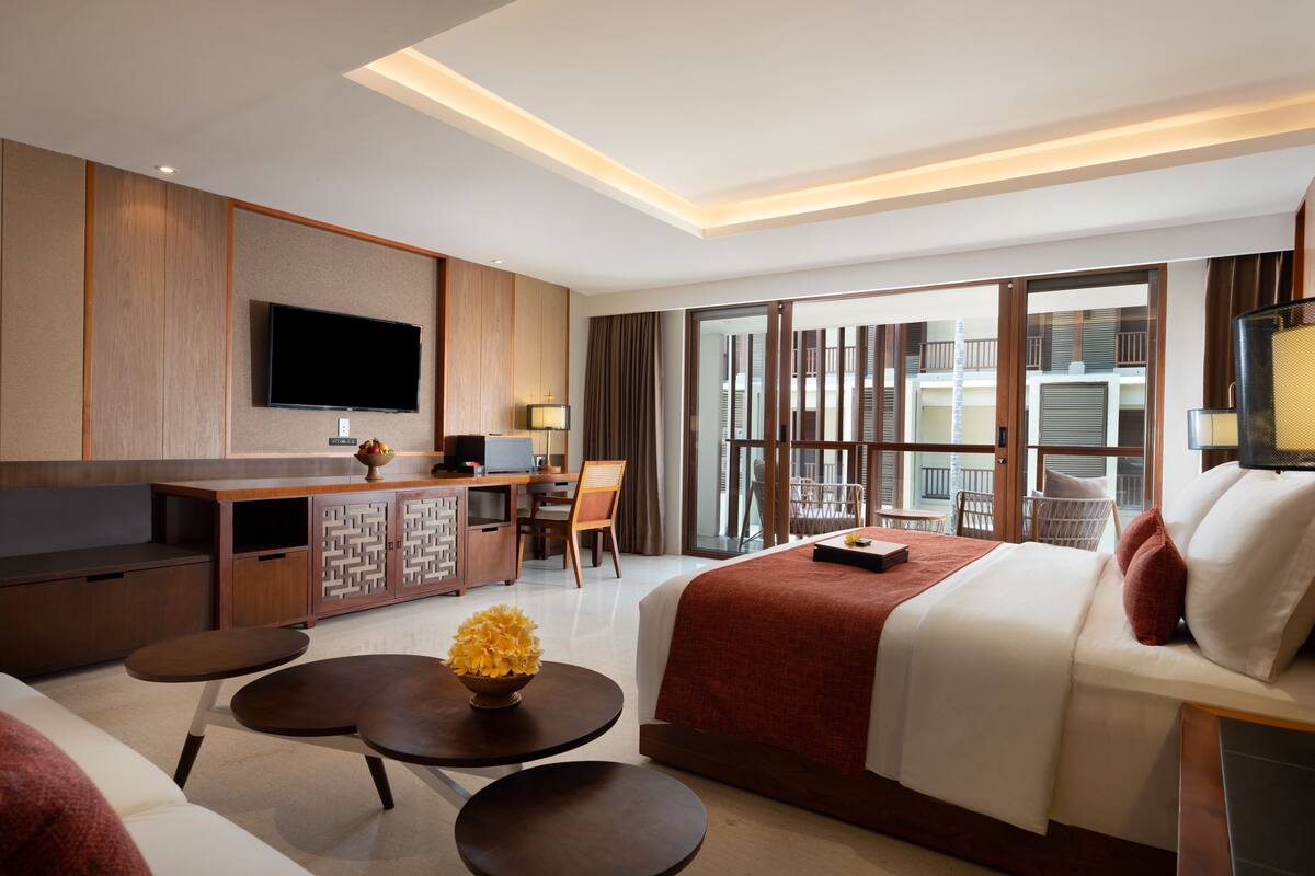 Habitación de hotel con cama, escritorio con computadora, televisión y balcón con vistas.