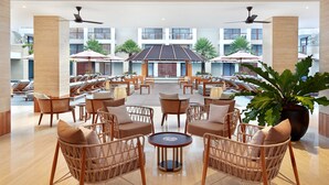 A spacious indoor area with wicker furniture, a central round table, and multiple ceiling fans. - The Bandha Hotel & Suites (Legian)
