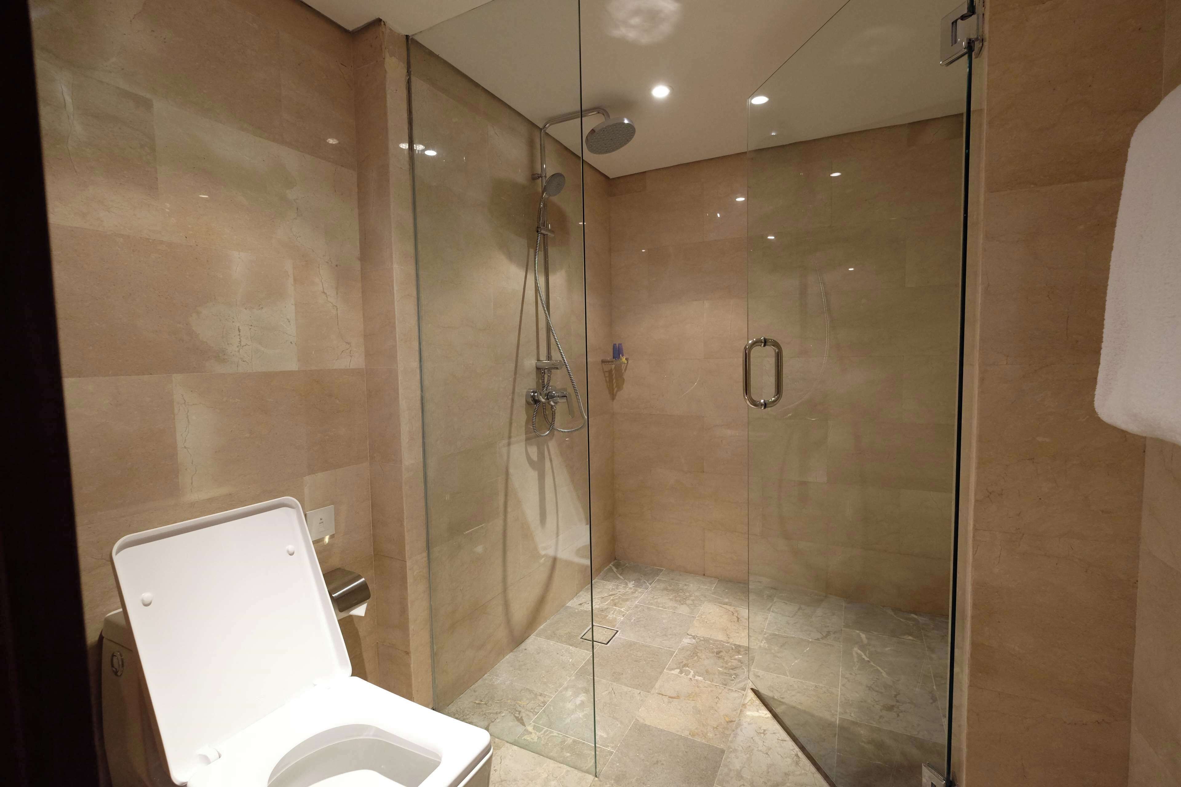 A modern bathroom with a glass-enclosed shower, a white toilet, and beige tiled walls.