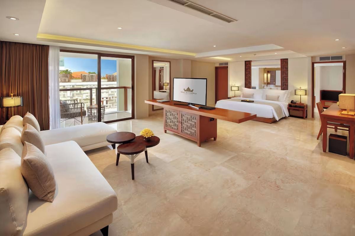 A hotel room with a bed, sofa, TV, and a balcony with outdoor furniture.