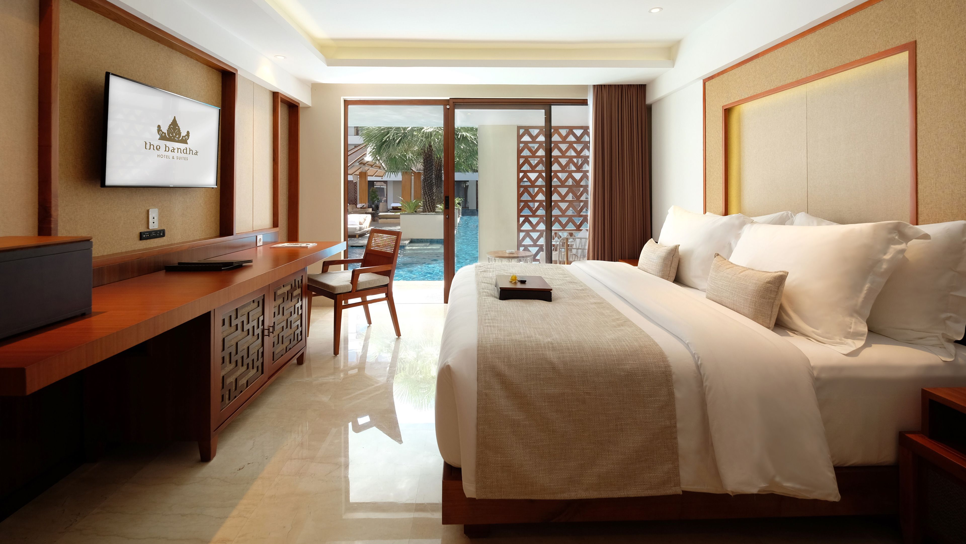 A hotel room with a bed, a desk, a television, and a view of an outdoor pool.