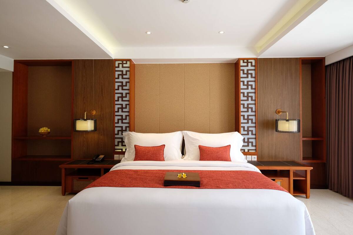 Habitación de hotel con una cama grande, dos mesitas de noche, un escritorio y un panel decorativo en la pared.