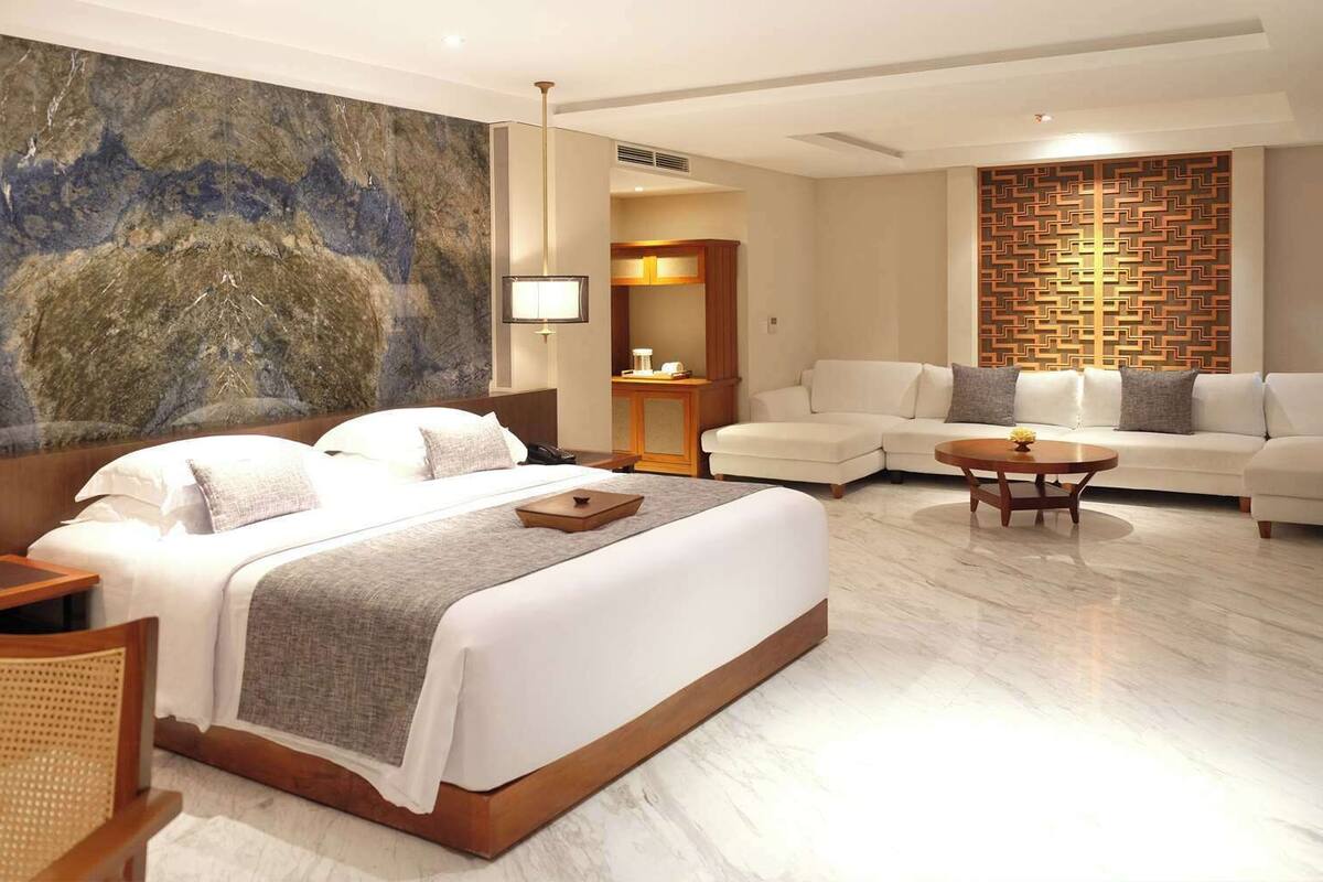 Una habitación de hotel moderna con una cama grande, un sofá, una mesa de centro y un muro decorativo.
