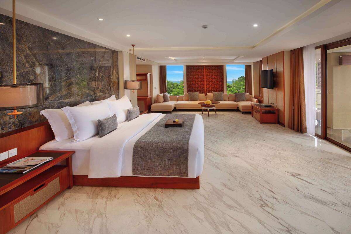 Amplia habitación de hotel con una cama grande, un sofá, un televisor y vistas a zonas verdes.