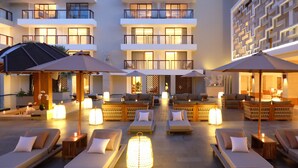 A rooftop lounge area with sun loungers, umbrellas, and ambient lighting. - The Bandha Hotel & Suites (Legian)