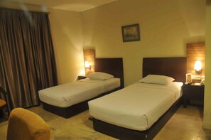 A hotel room with two single beds, a wooden headboard, a wall-mounted painting, and a curtain. - Losari Blok M  Hotel Jakarta (Jakarta)