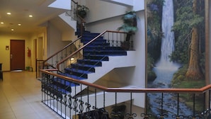 A staircase with blue steps and a metal railing, leading to a landing with a large waterfall mural. - Losari Blok M  Hotel Jakarta (Jakarta)