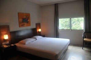 A hotel room with a large bed, two bedside lamps, a chair, and a window with a view of trees. - Losari Blok M Hotel Jakarta (Jakarta)