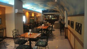 A restaurant with a ceiling mural, wooden tables, and black chairs. - Losari Blok M  Hotel Jakarta (Jakarta)