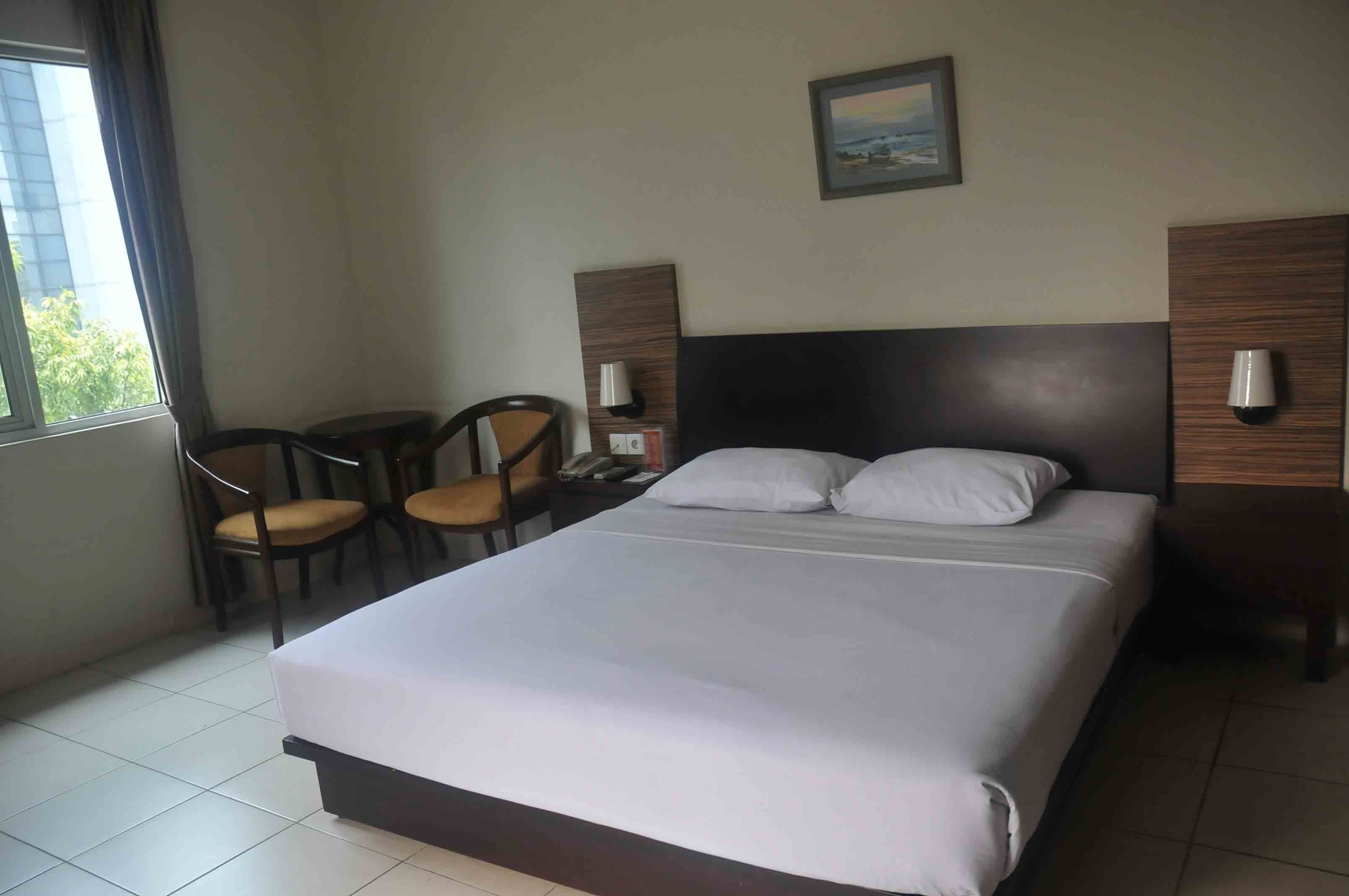 A hotel room with a large bed, two bedside tables with lamps, a chair, and a window with curtains.