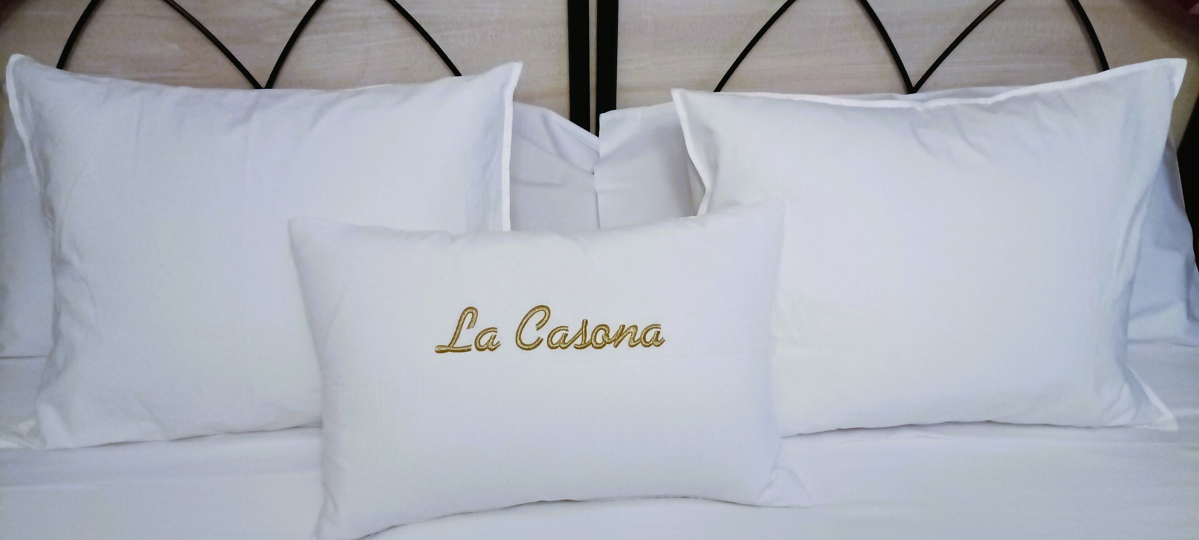 Ein Bett mit weißer Bettwäsche und einem Kissen, verziert mit "La Casona" in Gold.