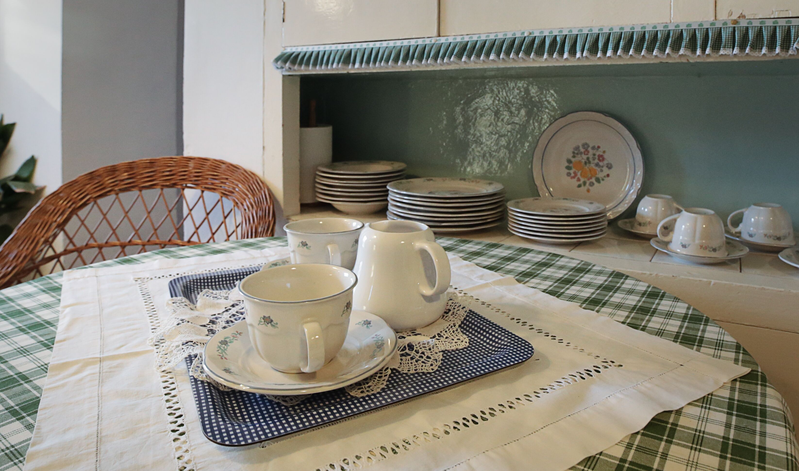 Una mesa de comedor con mantel a cuadros, un posavasos de encaje y una pila de platos y tazas.