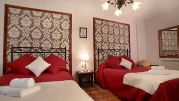 Habitación de hotel con dos camas, cada una con ropa de cama roja y almohadas blancas, una mesita de noche con una lámpara y un espejo en la pared.