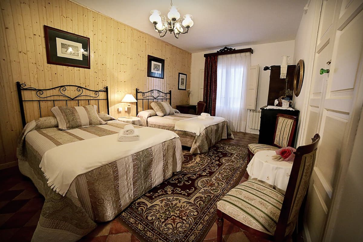 Quarto de hotel com duas camas, área de estar com uma poltrona, uma mesa e um espelho.