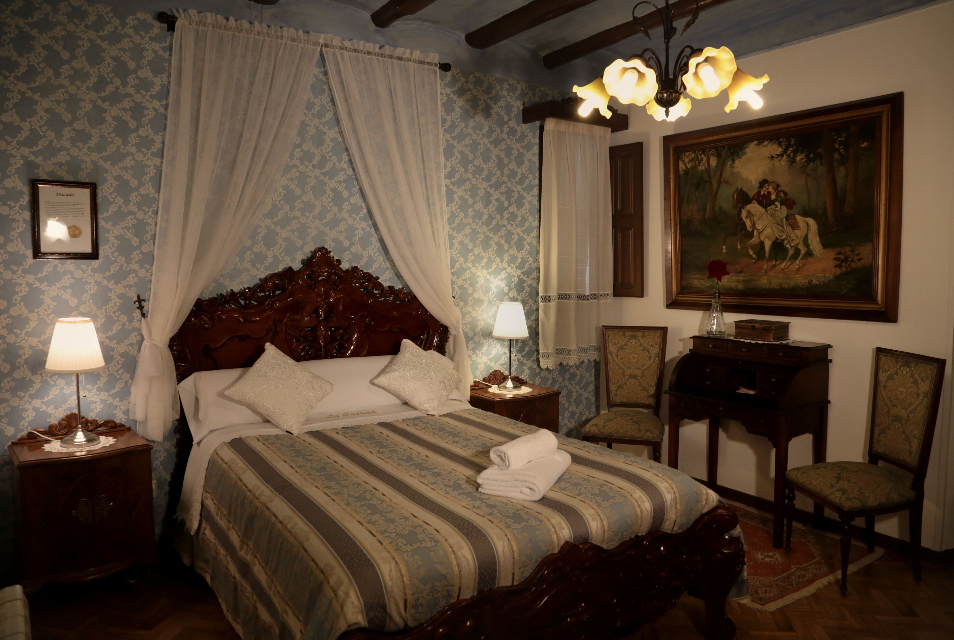 Een slaapkamer met een groot bed, twee nachtkastjes met lampen, een houten hoofdbord, een schilderij aan de muur en een stoel.
