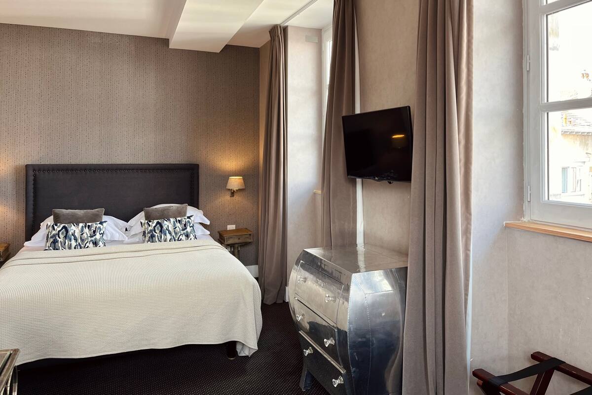 A hotel room with a large bed, a flat-screen TV mounted on the wall, a dresser, and a window with curtains.