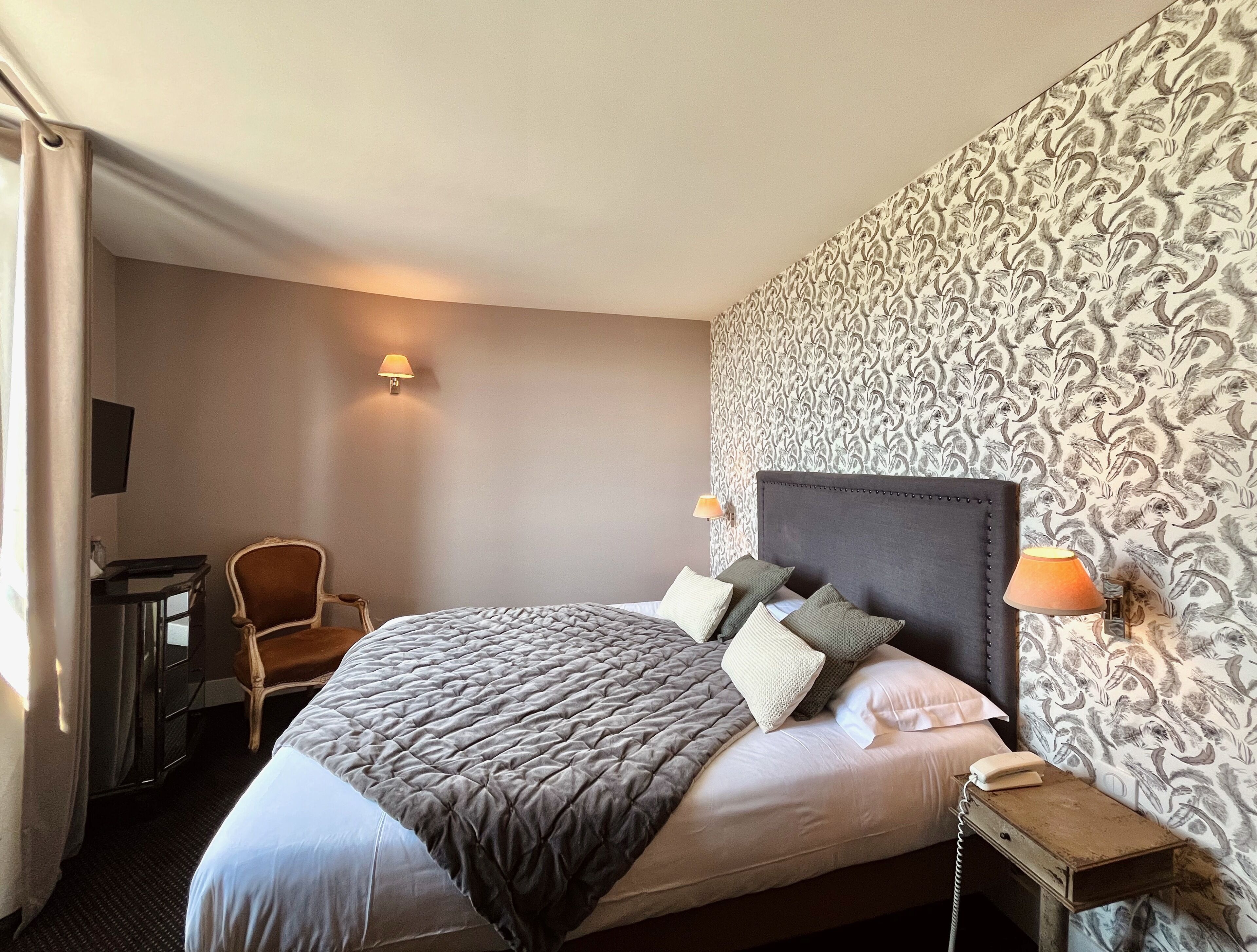A hotel room with a large bed, a desk, a chair, and patterned wallpaper.