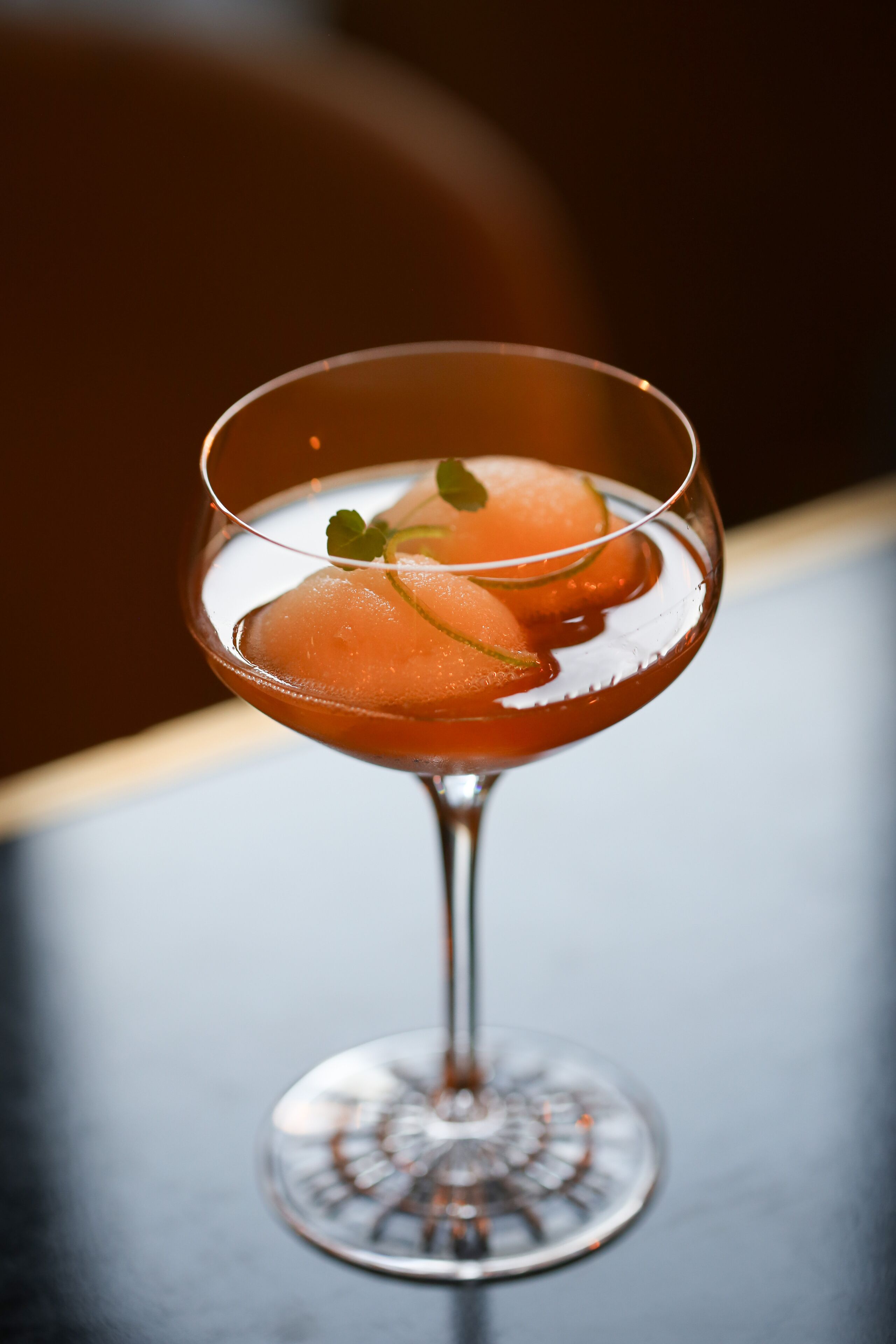 Un cocktail servi dans un verre à pied, agrémenté d’une garniture, posé sur une surface réfléchissante.