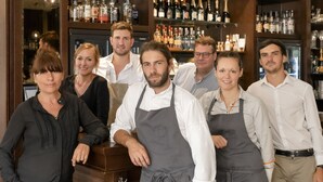 A group of people standing in a bar area with wooden cabinets and hanging pendant lights. - Hôtel des Basses Pyrénées (Bayonne)
