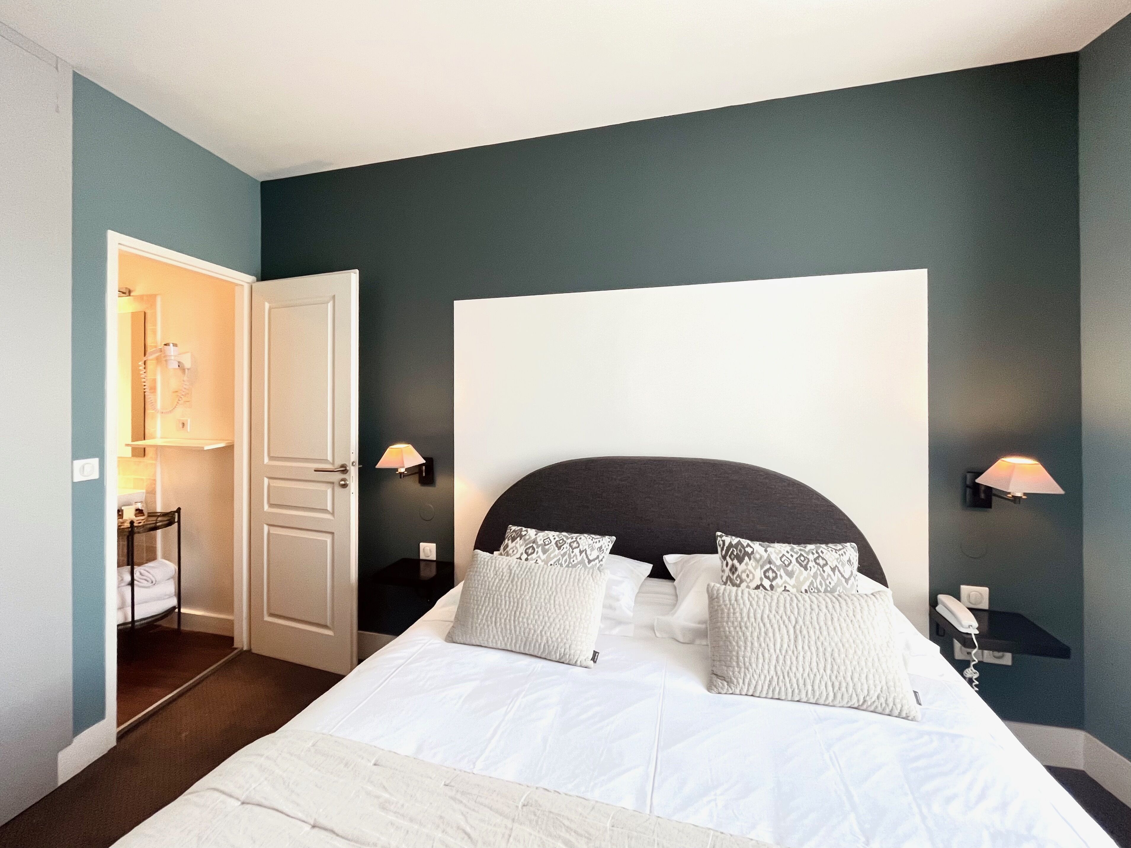 Une chambre à coucher avec un grand lit, deux lampes de chevet, une table de chevet et une porte donnant sur une salle de bain.