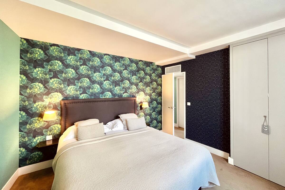 A bedroom with a bed, a nightstand, a wall-mounted lamp, and a door.