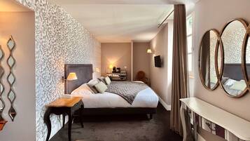 Quarto de hotel com uma cama grande, mesas de cabeceira, escrivaninha, cadeira, televisão e parede com padrão.