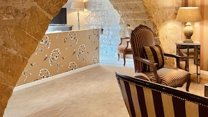A room with a stone wall, a striped armchair, a table with a lamp, and a floral wallpapered partition. - Hôtel des Basses Pyrénées (Bayonne)