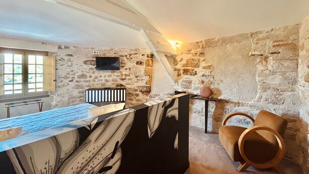 A rustic room with a stone wall, a desk with a keyboard, a chair, and a television mounted on the wall. - Hôtel des Basses Pyrénées (Bayonne)