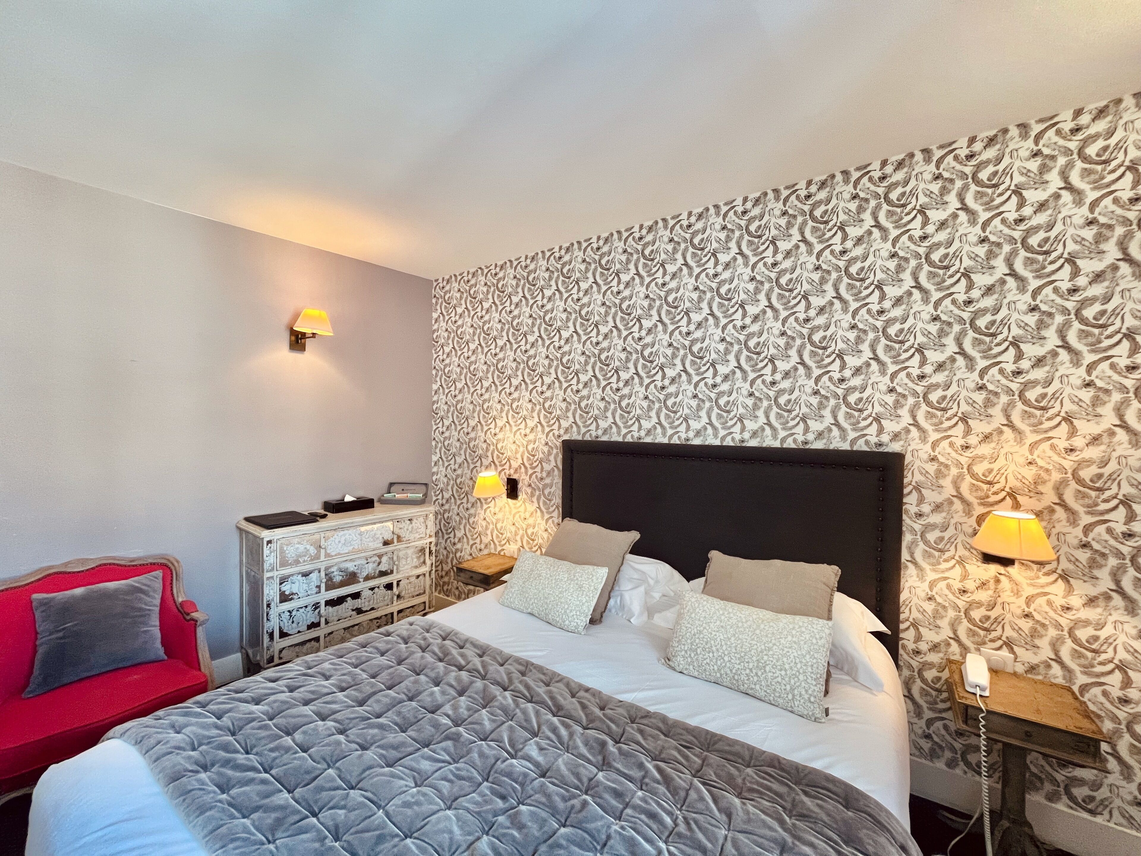 Une chambre à coucher bien rangée, avec un grand lit, un fauteuil rouge et une commode à tiroirs.