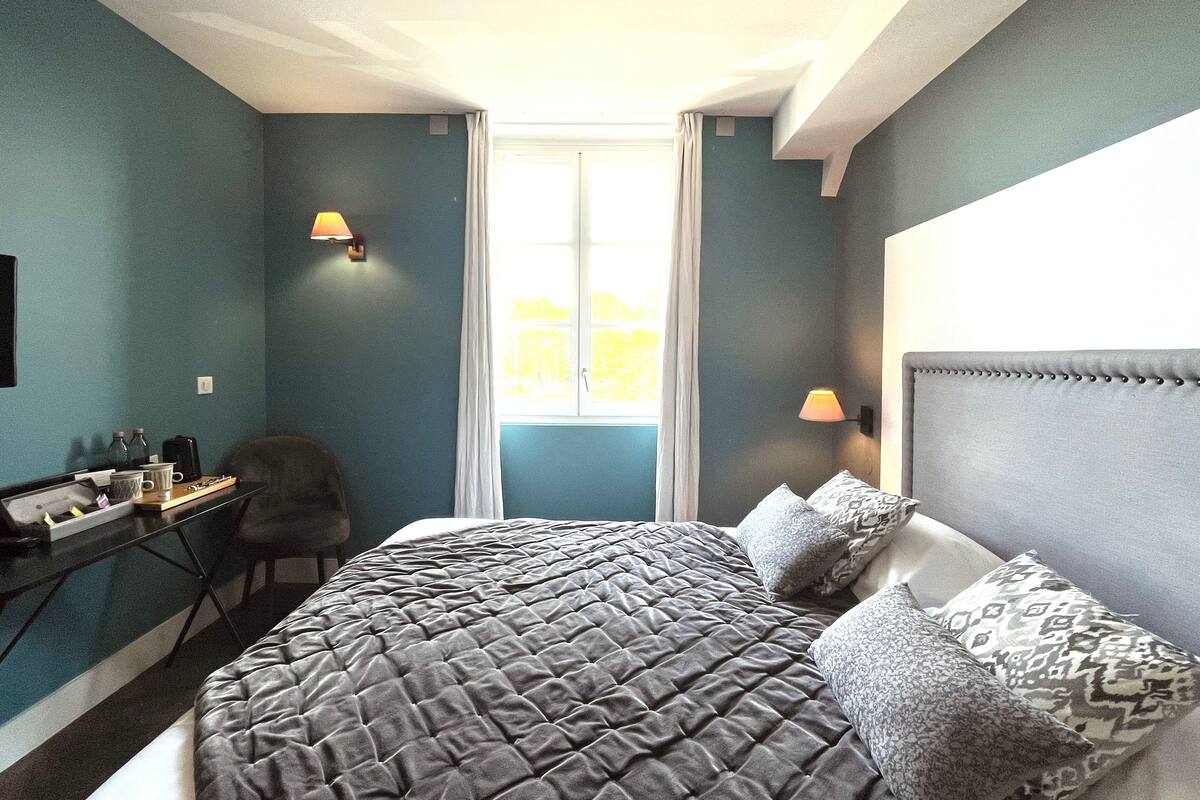 A bedroom with a large bed, a desk with a chair, and a window with curtains.