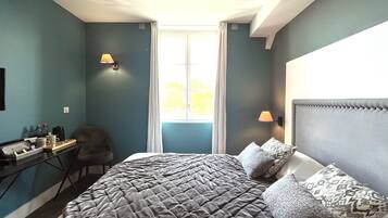 Quarto com uma cama grande, uma escrivaninha com cadeira e uma janela com cortinas.