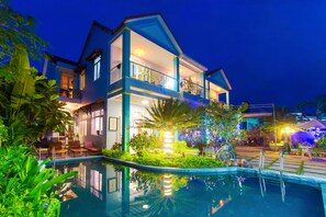 A two-story hotel with a swimming pool, outdoor seating, and a well-lit balcony. - Vy Hoa Hoi An Villas (Da Nang)