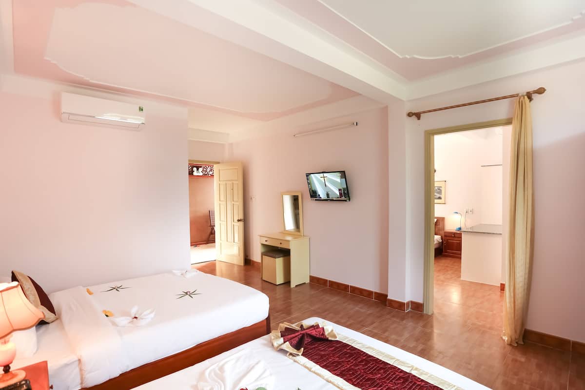 Une chambre d’hôtel avec deux lits, un bureau, une télévision et une salle de bain visible à travers une porte ouverte.