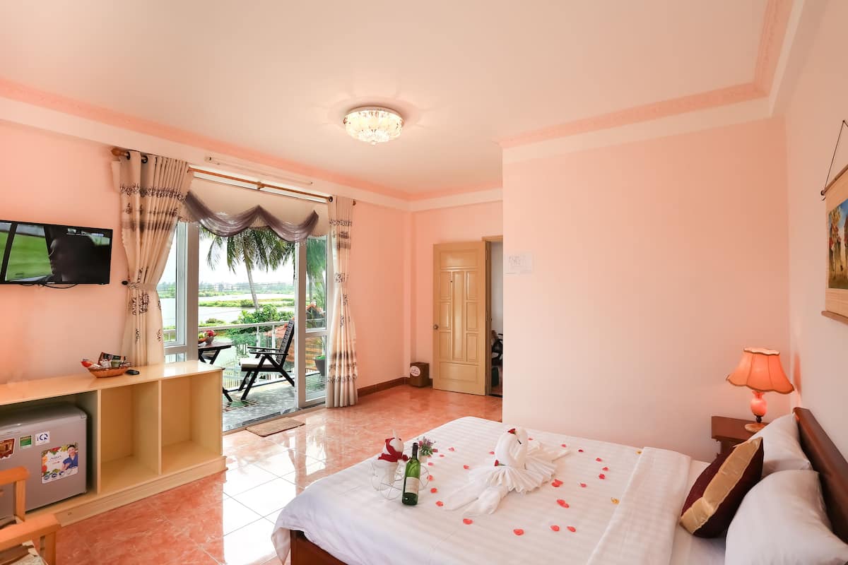 Une chambre d’hôtel avec un lit, une télévision, un bureau et un balcon offrant une vue sur les palmiers.