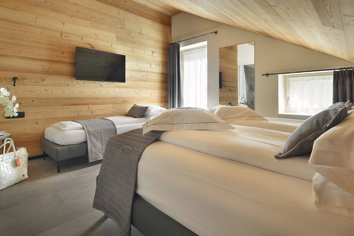 A cozy bedroom with wooden walls, a flat-screen TV, two beds, a window, and a small table with a plant and a bag.