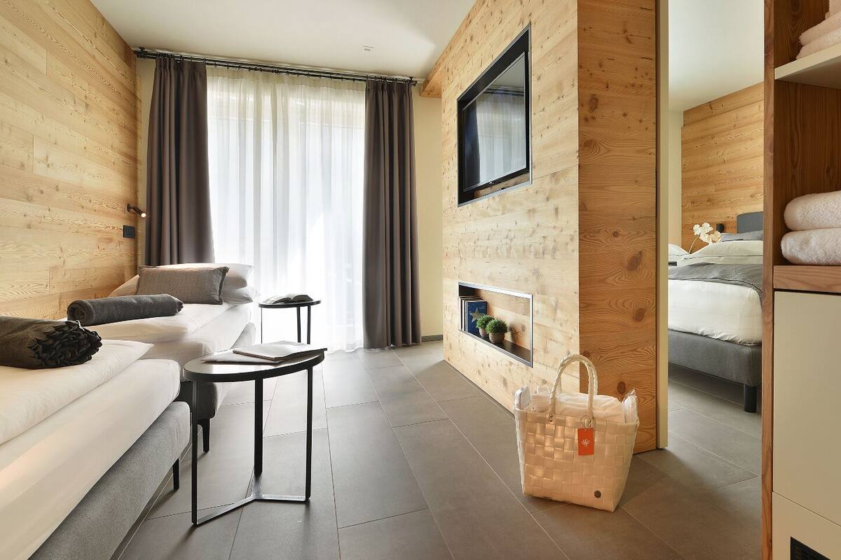 A modern hotel room with a wooden interior, a sofa, a small table, a bed, and a wardrobe.