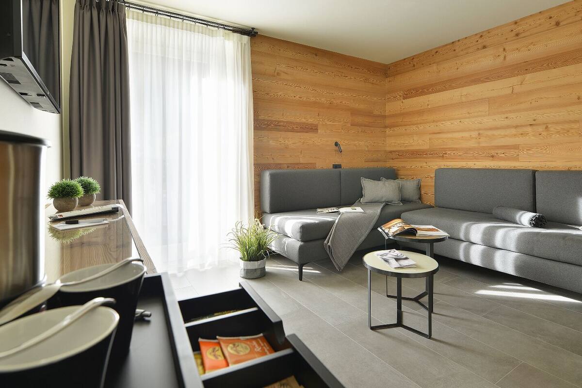 A modern living room with a grey sofa, a small side table, and a kitchen area with a stainless steel appliance.