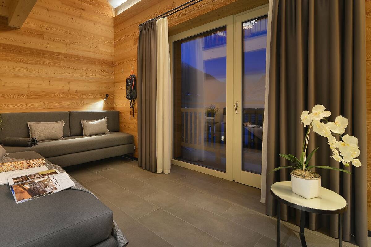 A modern living room with a grey sofa, a small table with a plant, and a sliding glass door leading to an outdoor area.