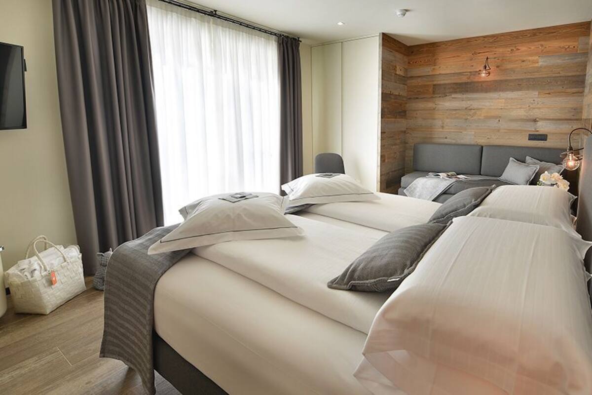 A hotel room with a modern design, featuring a large bed with multiple pillows, a bedside table, a TV mounted on the wall, and a wooden accent wall.