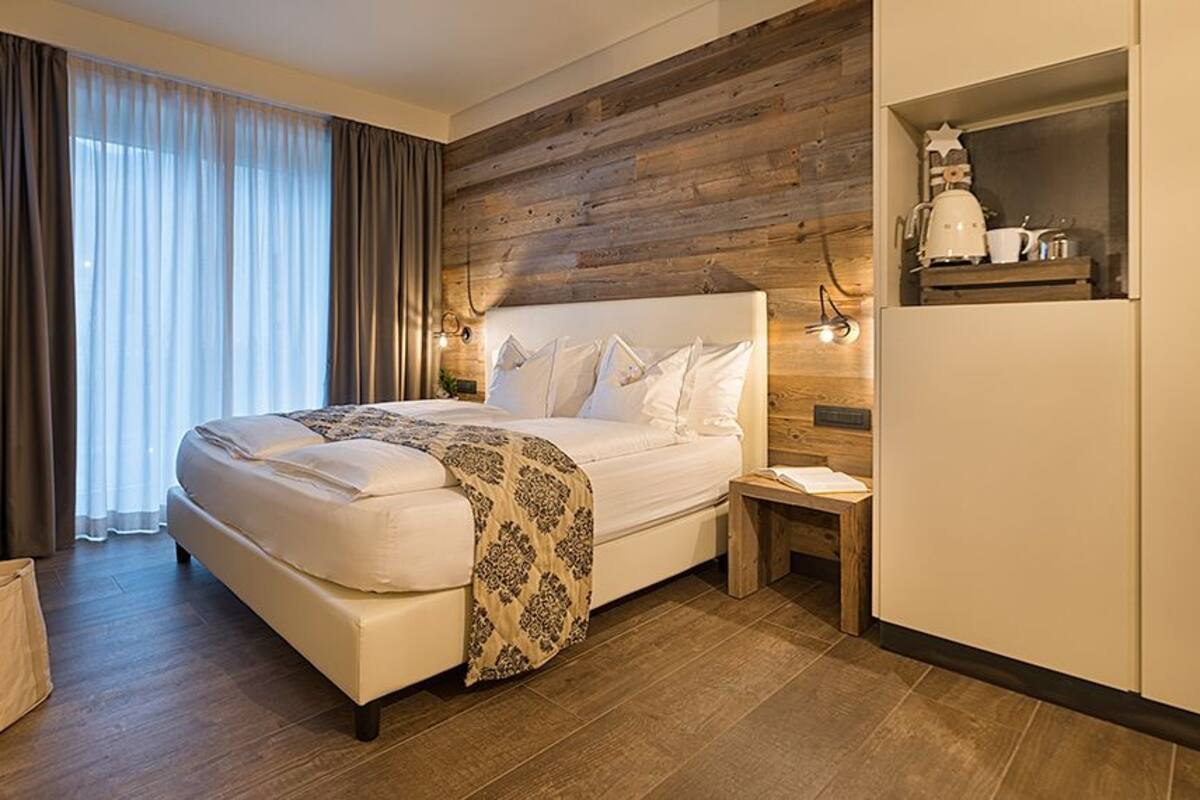 A hotel room with a bed, wooden panel wall, curtains, a nightstand, and a small cabinet with a star decoration.