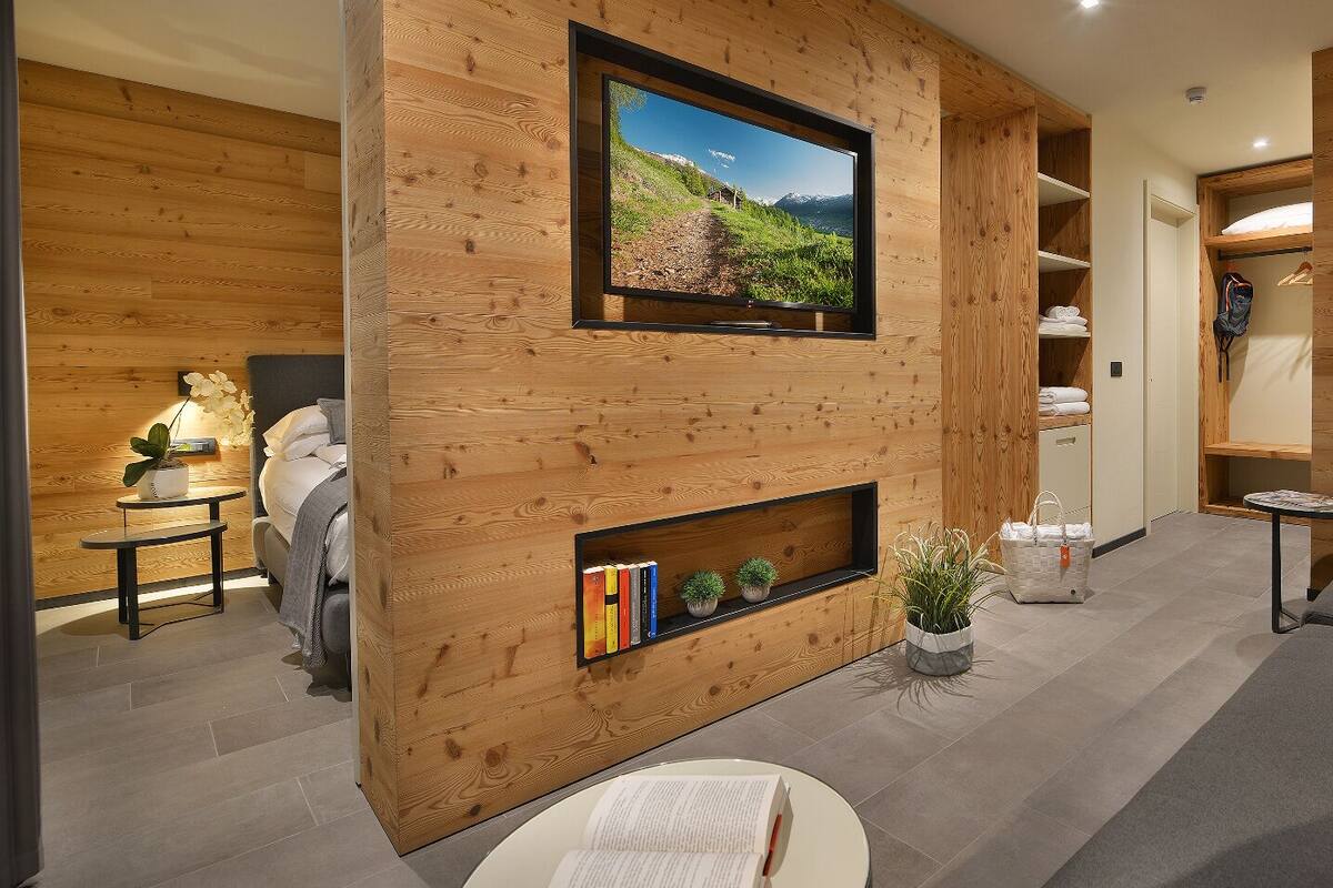 A modern living room with a wooden interior, a mounted TV, a sofa, and a bookshelf with books and plants.
