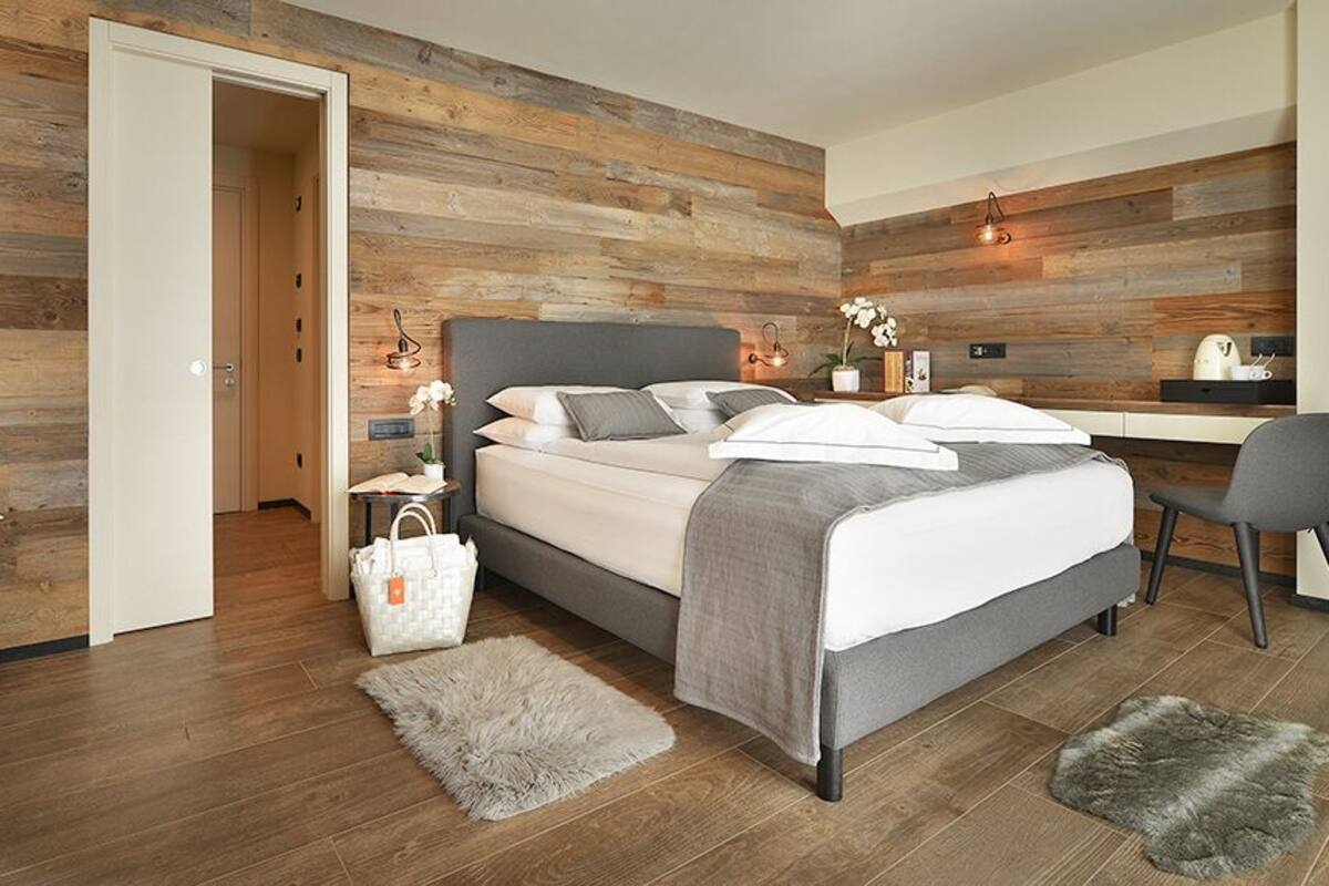 A modern bedroom with a wooden wall, a bed with grey bedding, a desk, and a chair.