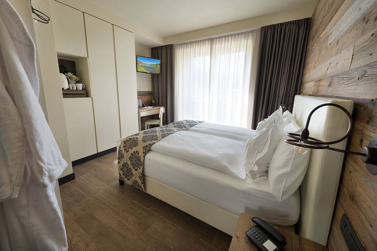 A hotel room with a bed, a desk, a TV, and a wooden wall.