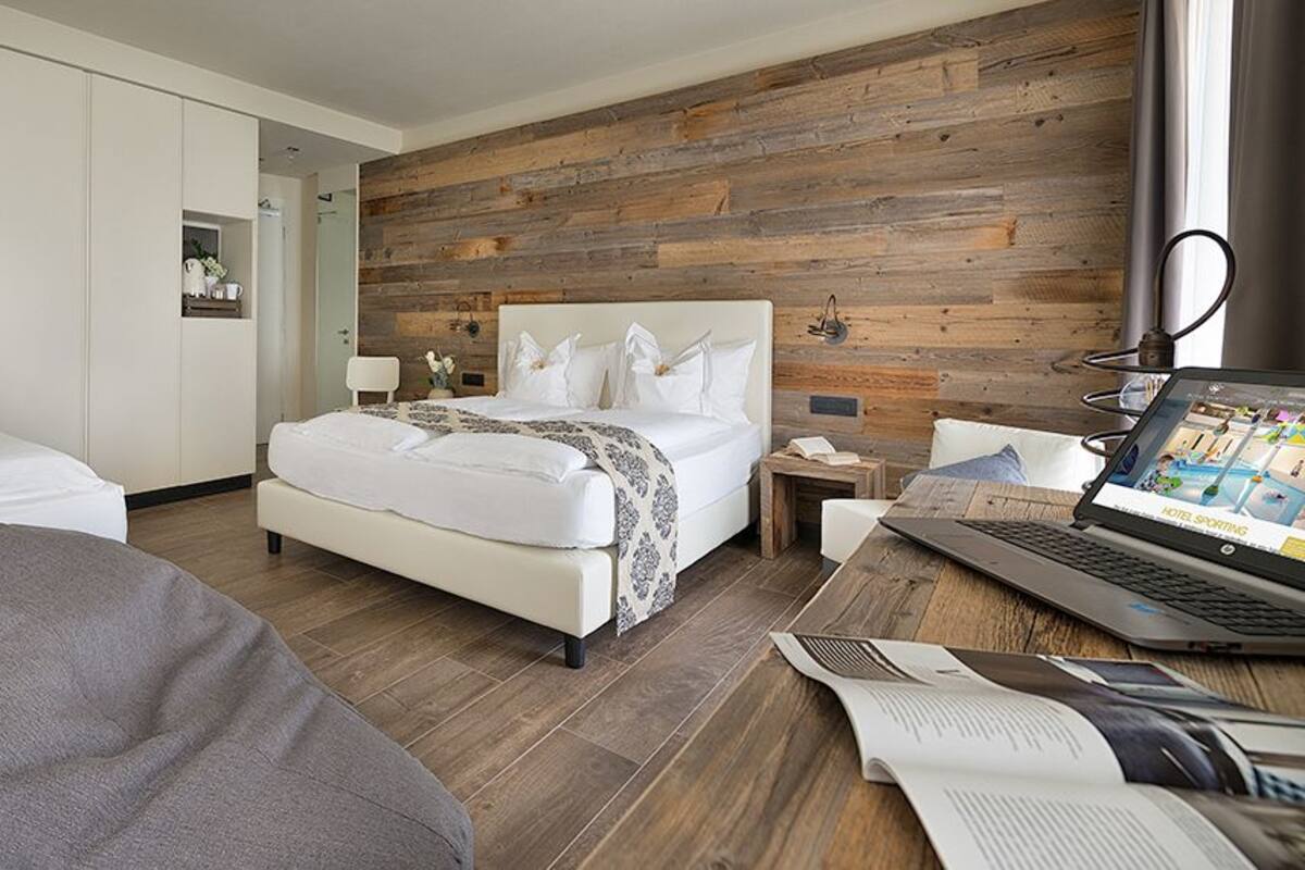 A modern hotel room with a wooden accent wall, a large bed, a desk with a laptop, and a comfortable seating area.