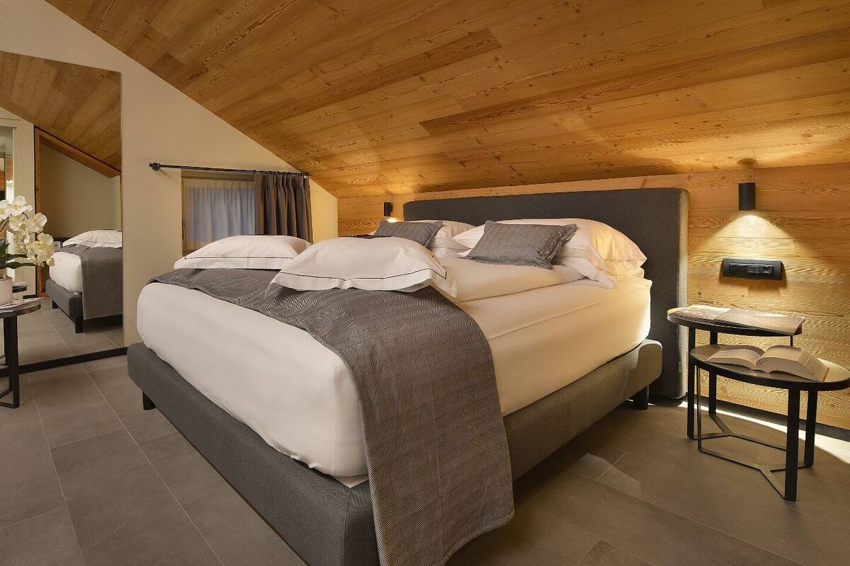 A modern bedroom with a large bed, bedside tables, a mirror, and a wooden ceiling.