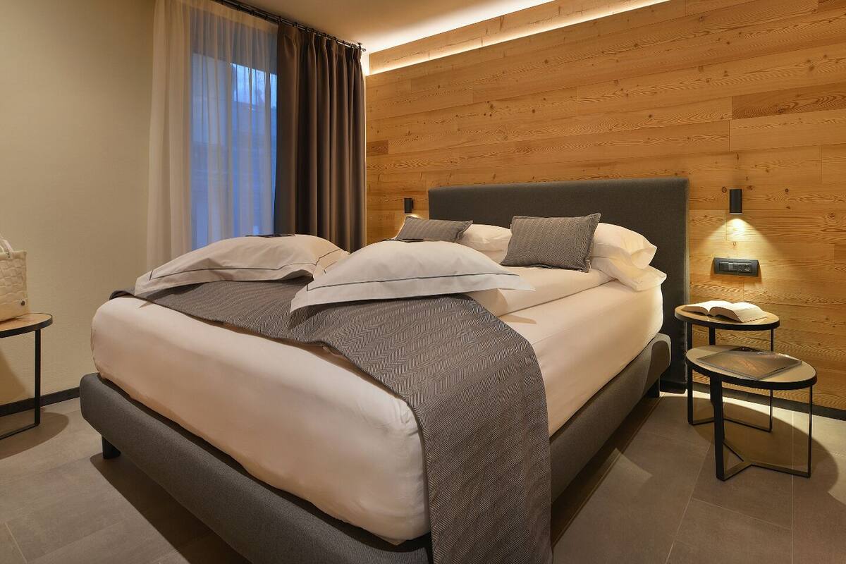 A modern hotel room with a large bed, a small bedside table with a lamp, and a wooden accent wall.