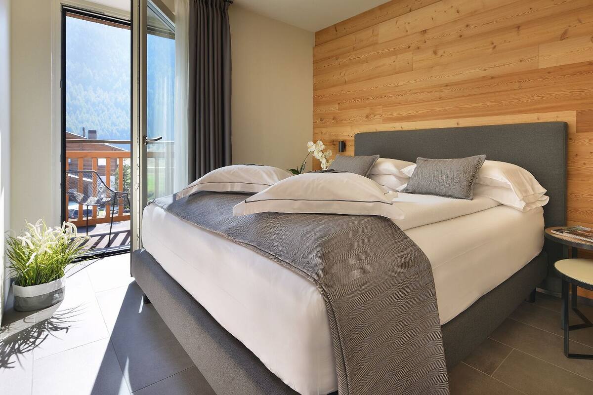 A modern bedroom with a large bed, a small bedside table, and a view of a balcony.