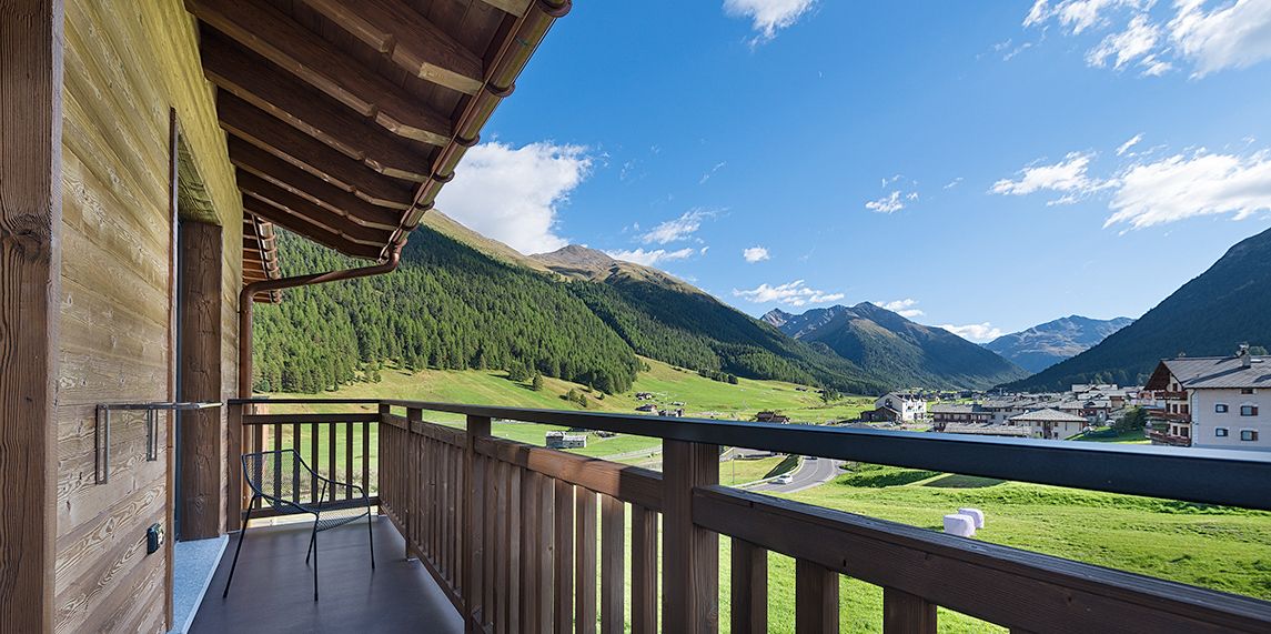 A wooden balcony with a view of a mountain landscape and a village below.
