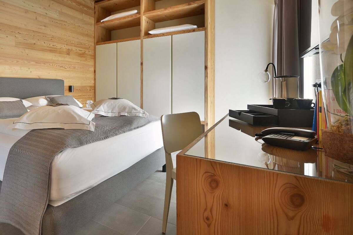 A modern hotel room with a large bed, a wooden desk, and a wardrobe.